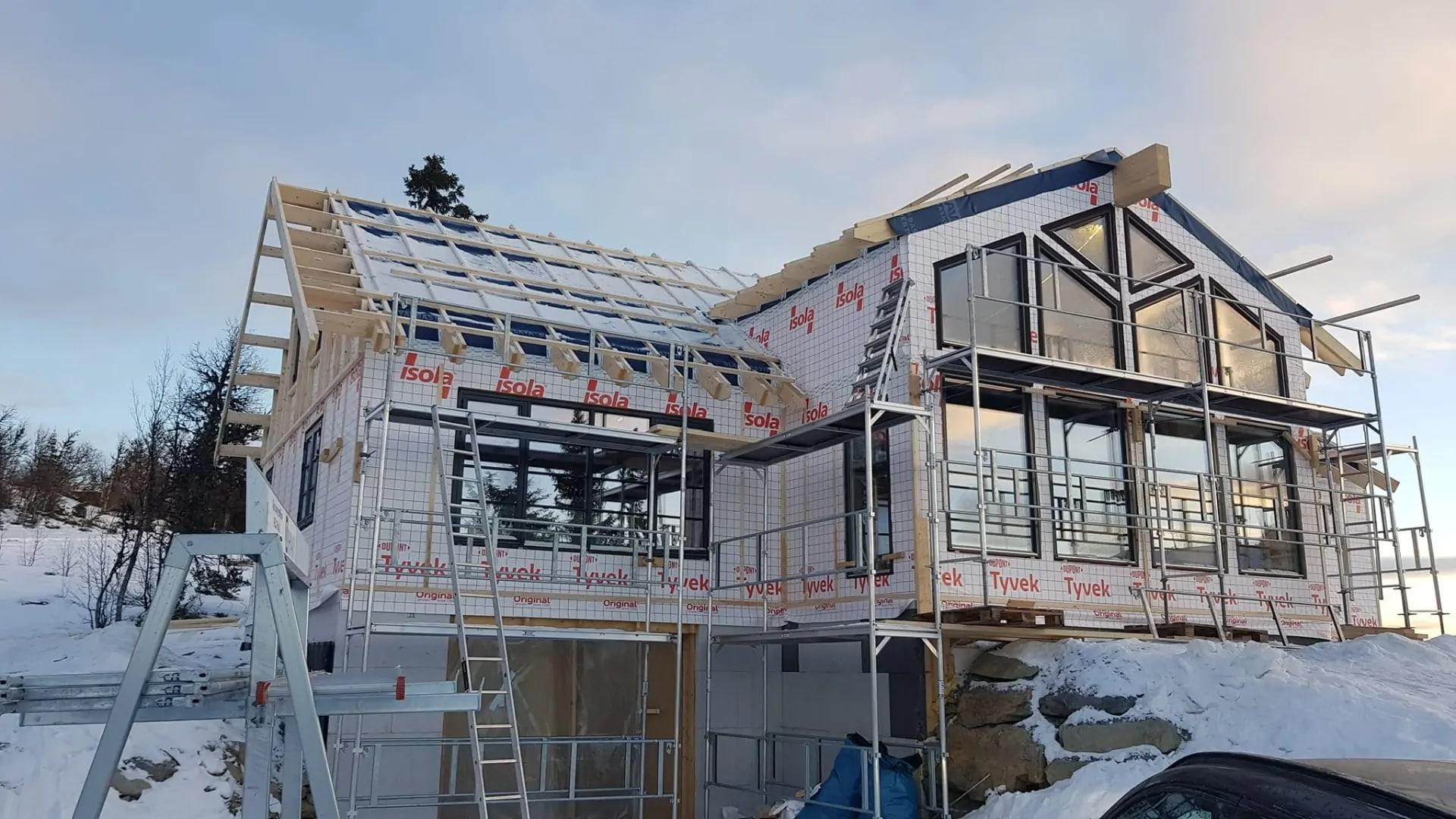 A large cabin going up in the snow, wrapped in wind barrier, with scaffolding along the side