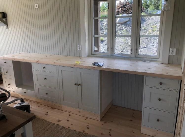 Built-in white cupboards and a desk under a window, on a pine floor