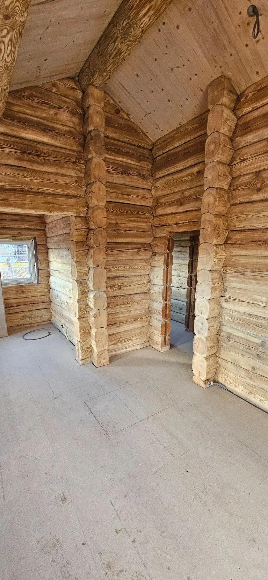 Inside a new log building: bare log walls and a doorway, no floor laid yet