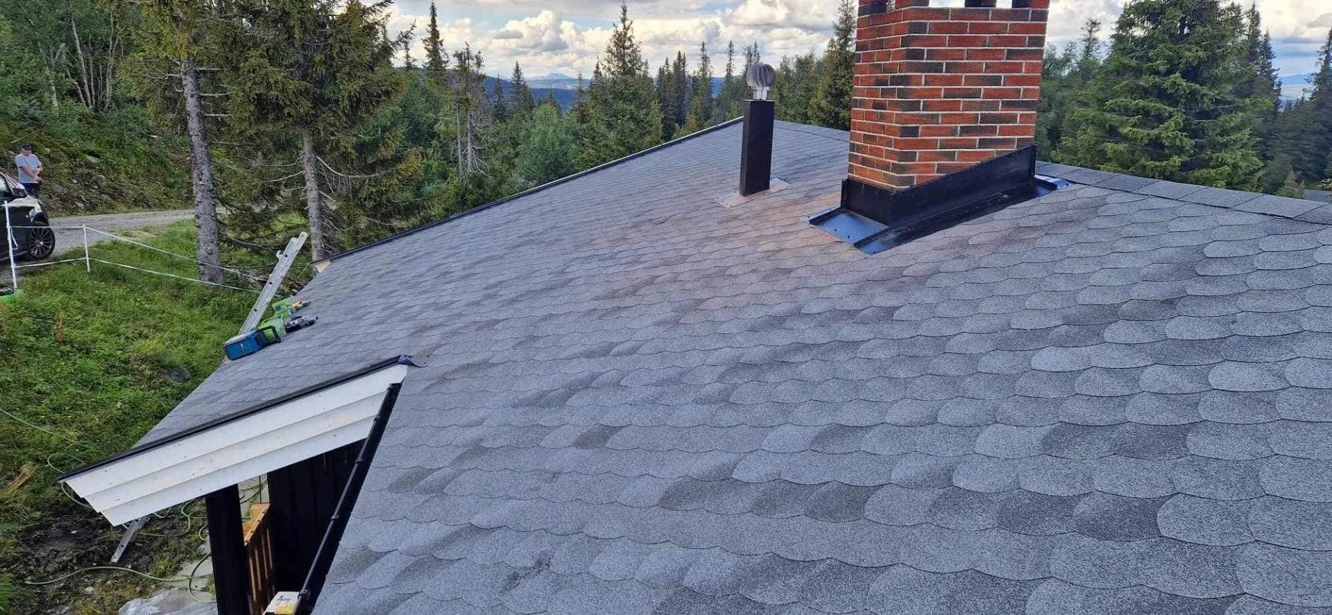 A grey shingle roof with a brick chimney and new flashing along the edge